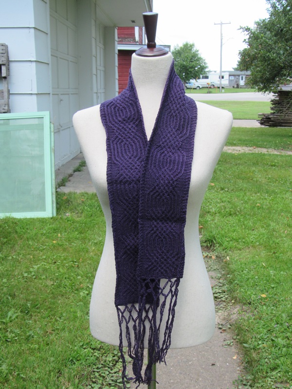 hand knit dark purple scarf with a narrow cabel pattern and fringe